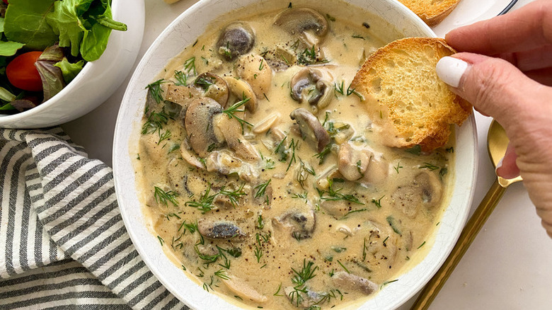 Dunking crusty bread into bowl of creamy mushroom soup