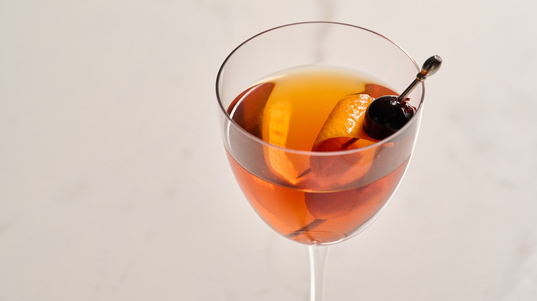Rob Roy cocktail in long-stemmed glass, garnished with orange peel and luxardo cherry