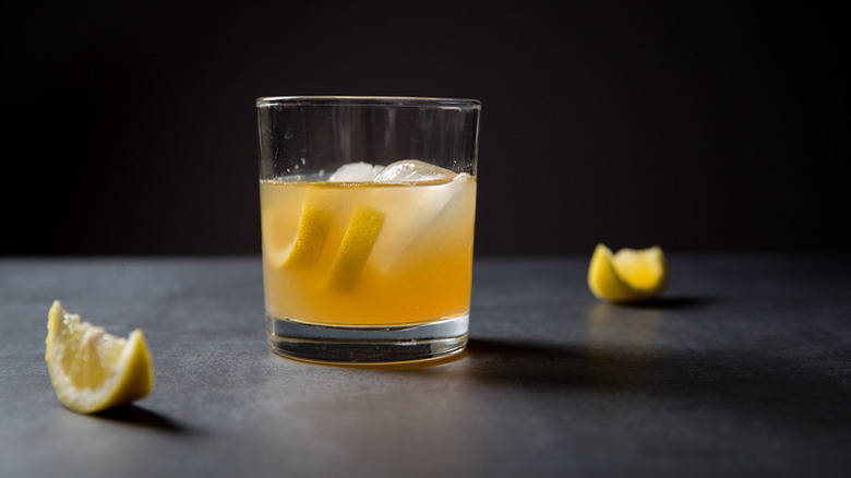 Gold rush cocktail in glass with lemon slices and ice