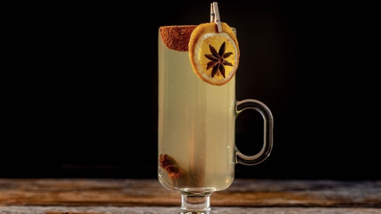 Hot toddy cocktail in tall handled glass, garnished with dried orange and star anise