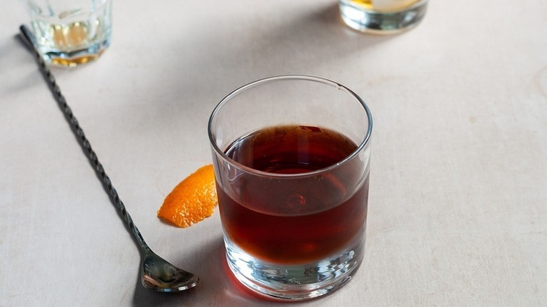 Manhattan cocktail in glass next to metal stirrer and piece of orange peel