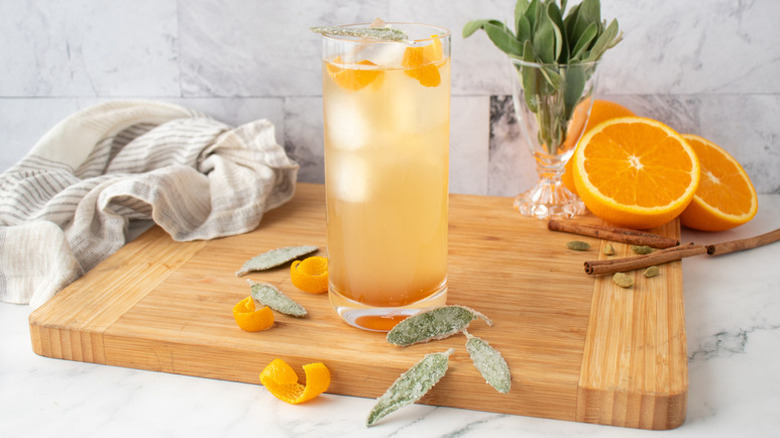 Whiskey ginger cocktail in tall glass, garnished with orange twists and candied sage