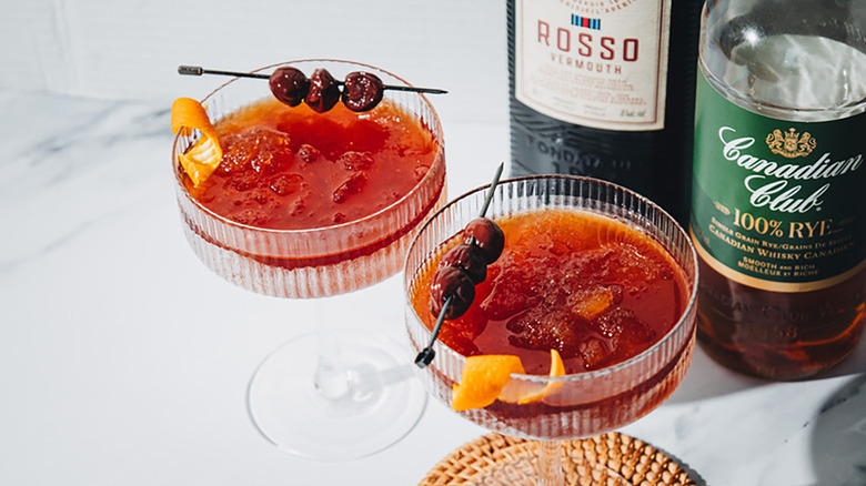 Frozen manhattan cocktails in coupe glasses, each garnished with skewered amarena cherries and an orange twist