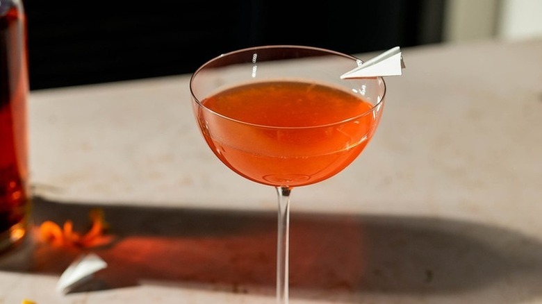 Paper plane cocktail in long-stemmed glass, garnished with mini paper plane