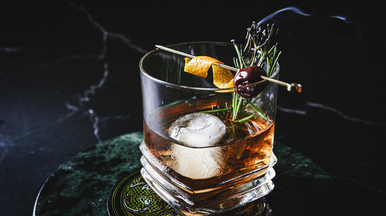Old fashioned cocktail with ice, garnished with orange twist and luxardo cherry