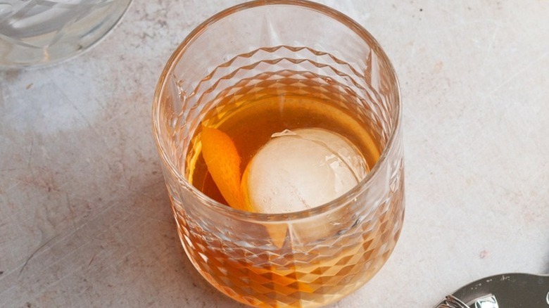 Old fashioned cocktail in glass with ice and orange peel