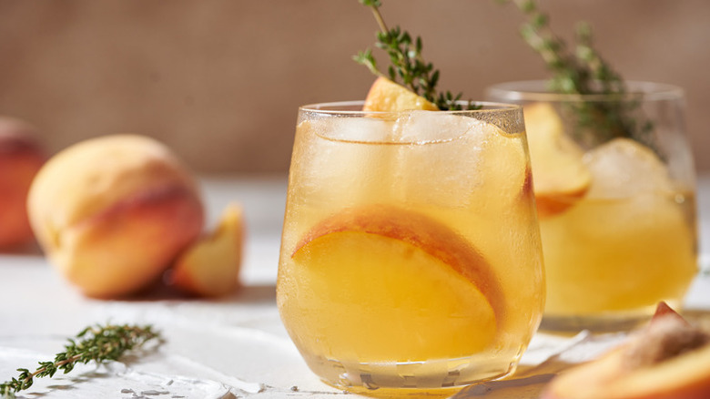 Peach whiskey cocktails in glasses, garnished with fresh thyme sprigs