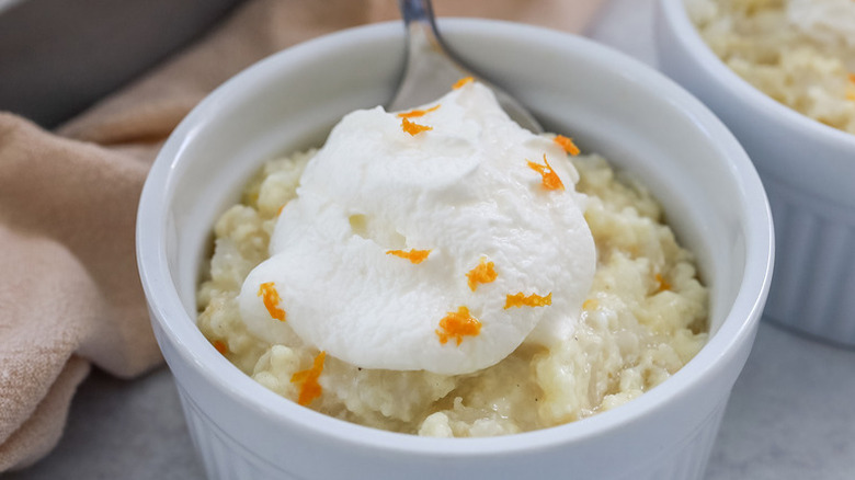 Rice pudding in small white bowl, topped with cool whip and orange zest