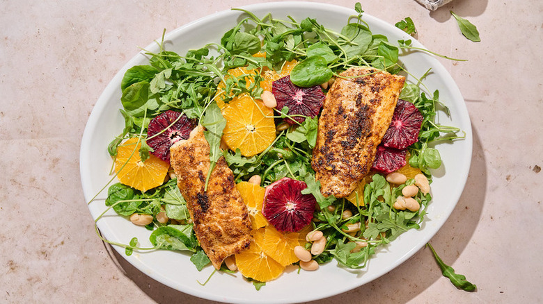 Plate of leafy green salad with blackened cod and fresh orange slices