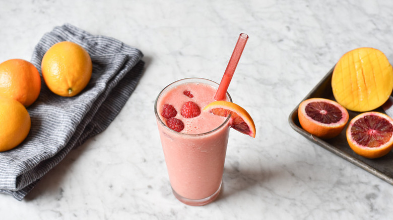 Blood orange smoothie in glass, garnished with fresh raspberries and a blood orange slice