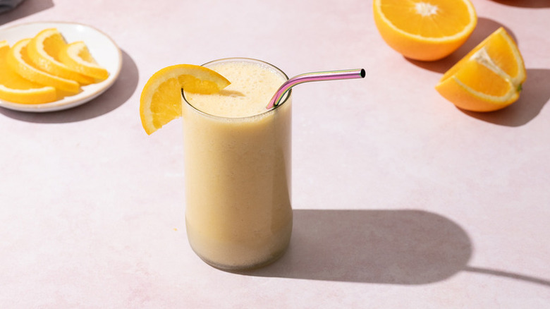 Creamy orange smoothie in glass with metal straw, garnished with orange slice