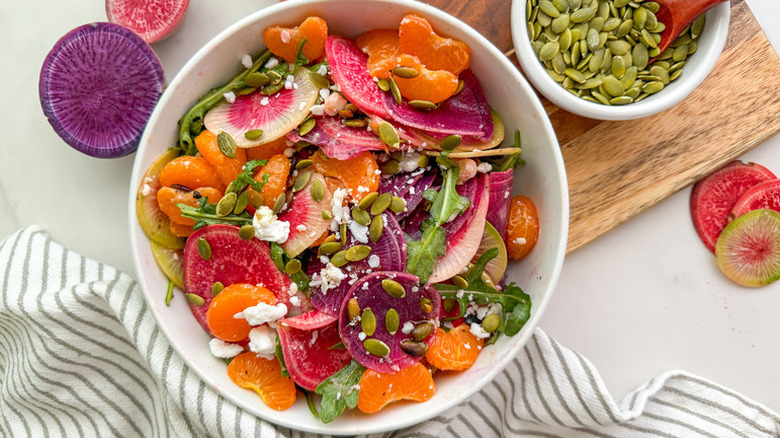 Bowl of colorful radish and mandarin salad, garnished with pumpkin seeds and crumbled feta