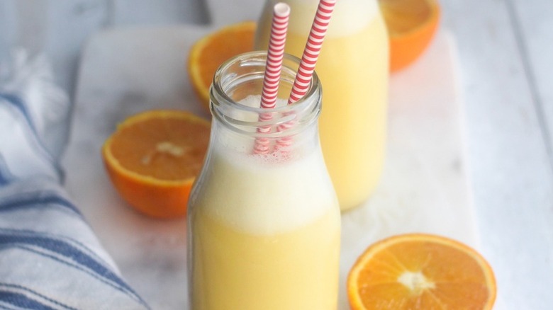 Creamy orange Julius drink in glass bottle with stripy red and white straws