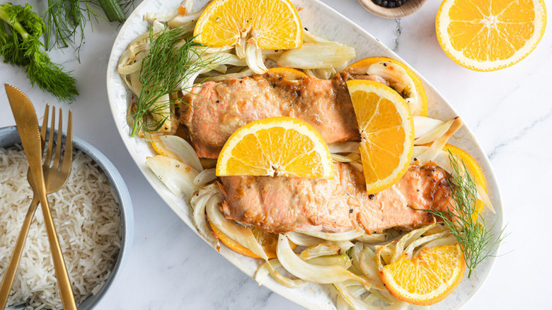 Roasted salmon and fennel on plate with orange slices and fresh dill sprigs