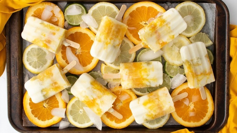 Creamy citrus popsicles on parchment-lined baking sheet with frozen lemon, lime, and orange slices