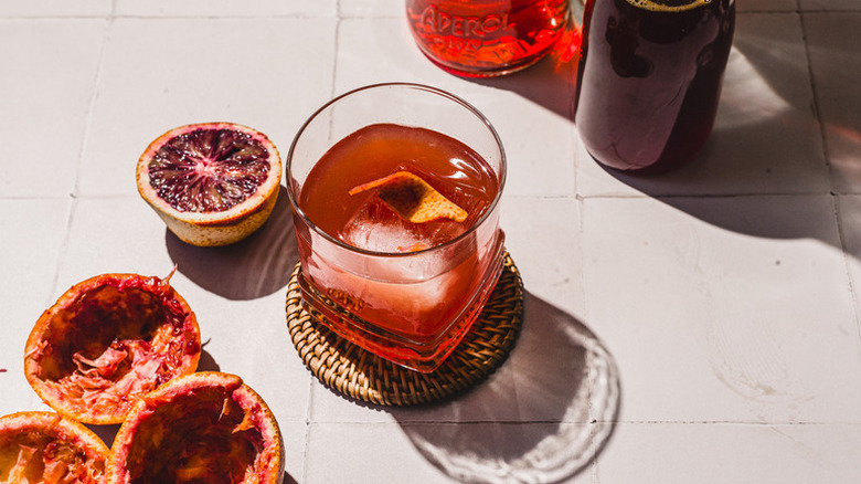 Blood orange screwdriver cocktail in glass, next to fresh blood orange halves