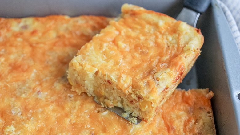 Scooping portion of cornbread casserole from baking dish