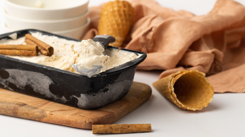 Eggnog ice cream in loaf pan next to ice cream cones and cinnamon sticks
