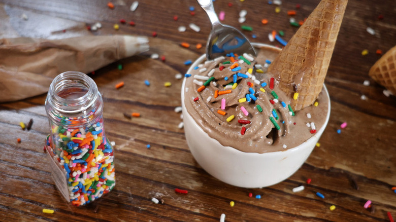 Soft serve ice cream in white bowl with ice cream cone and rainbow sprinkles