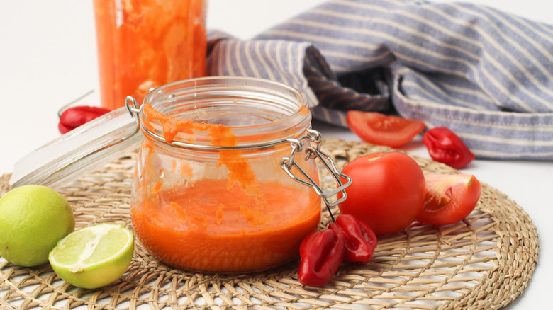 Chili-lime hot sauce in open glass jar next to fresh chiles, tomatoes, and limes