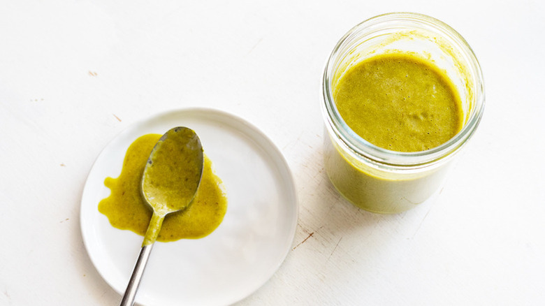 Jar of green hot sauce next to plate with sauce-covered spoon