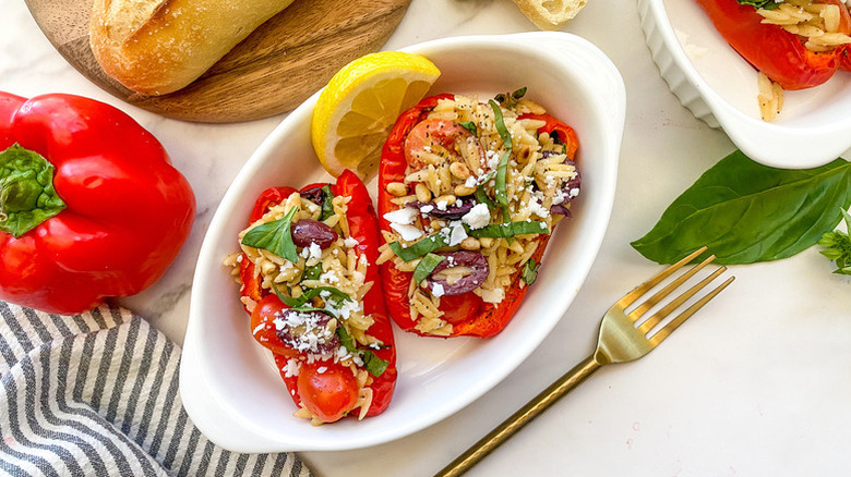 Feta and orzo-stuffed peppers in a white dish with a lemon wedge