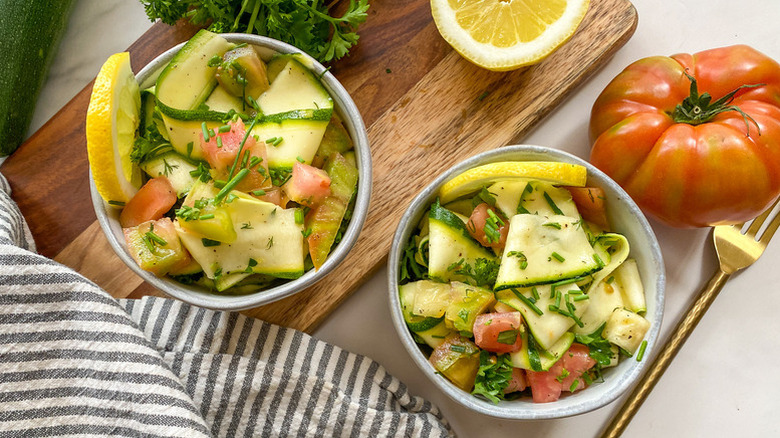 Two bowls of zucchini ribbon salad with tomatoes and lemon wedges