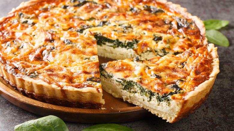 Sliced spinach quiche on a wooden serving plate