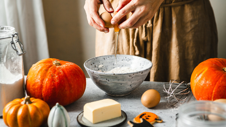 A person cracking eggs in a bowl in an autumnal baking scene
