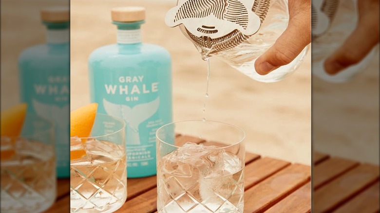 A hand pouring a cocktail with a bottle of Gray Whale gin in the background.