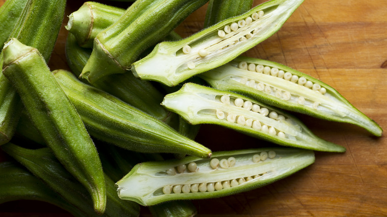 Raw green okra, some whole and others halved with visible seeds