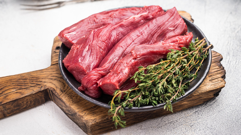 Raw tenderloin cut of lamb displayed alongside fresh herbs