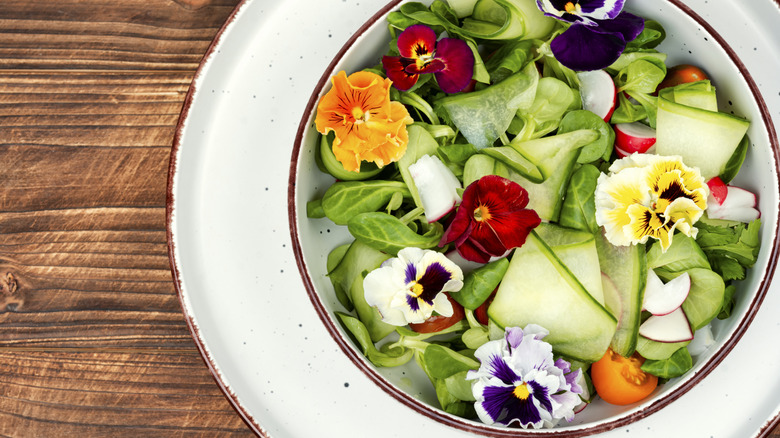 Colorful edible flowers in a bowl of green salad