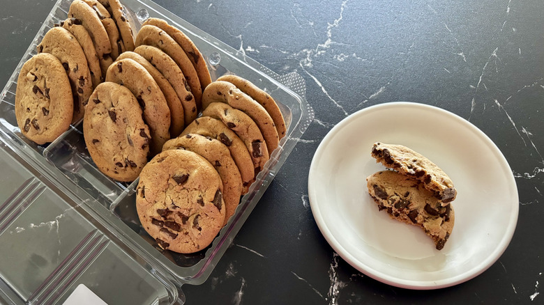 Costco chocolate chip cookies in container next to cookie split in half on plate