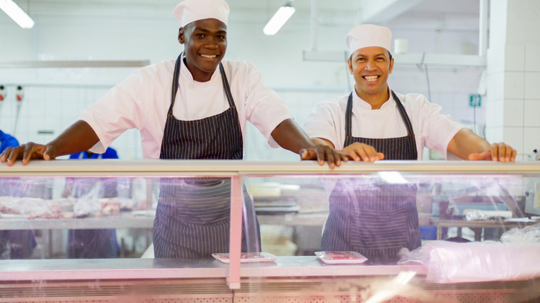 Two butchers smiling and standing behind a counter