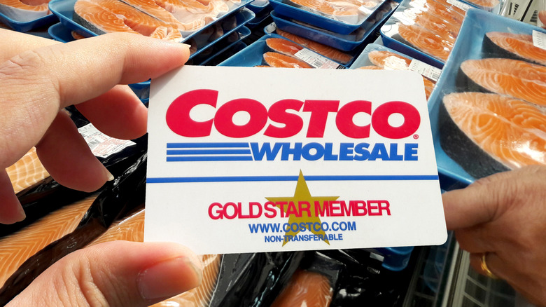man holding Costco card in front of fridge of packaged salmon filets