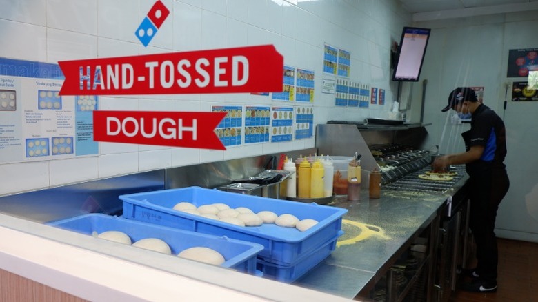 A sign reading hand-tossed dough at Domino's with an employee preparing pizza in the background