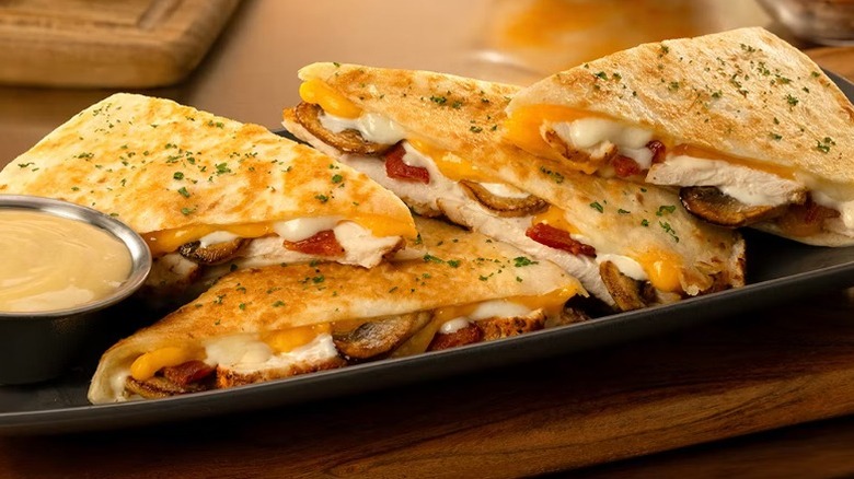 A beauty shot of Outback's Alice Springs Chicken Quesadilla with honey mustard sauce on a black platter sitting on a wooden table and background