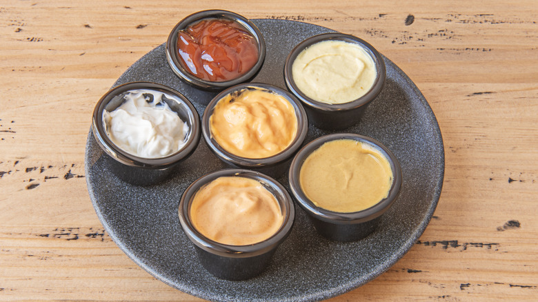 A black plate with an assortment of dressings in ramekins sitting on a wooden table