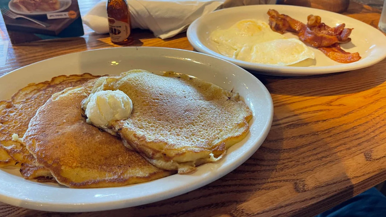 Cracker Barrel's breakfast items on a wooden table with a tiny bottle of maple syrup in the background