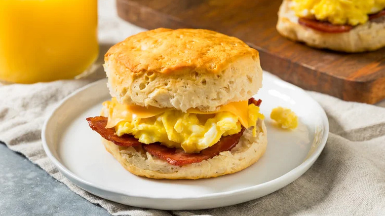 Bacon, egg, and cheese breakfast sandwich on plate beside orange juice