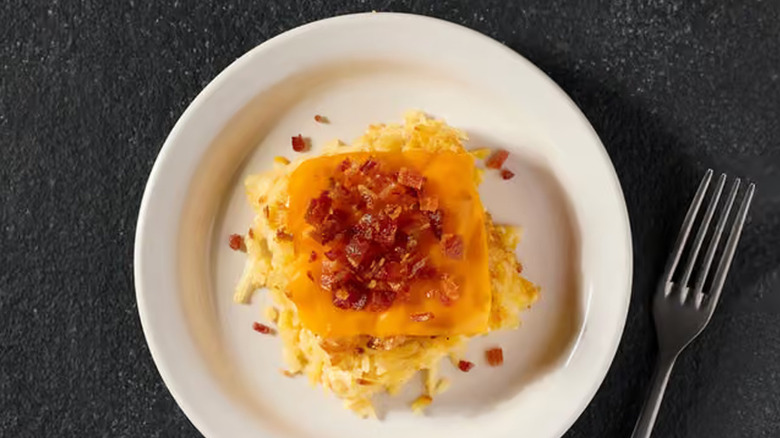 A plate of the loaded hash brown casserole sitting in a white dish on a blue and white background with a fork beside it