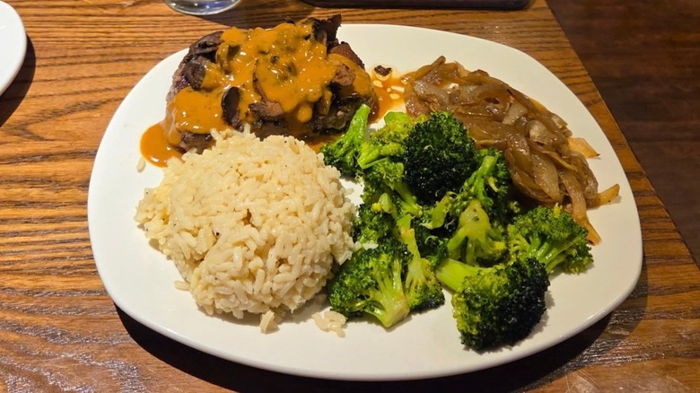 A plate of steak with mushrooms and onions, rice, and broccoli from Outback