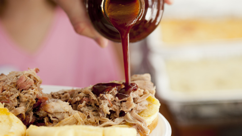Barbecue sauce being poured onto a pulled pork sandwich