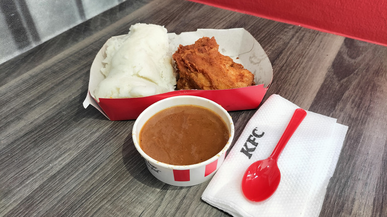 A takeout container of KFC chicken, mashed potatoes, and gravy on table