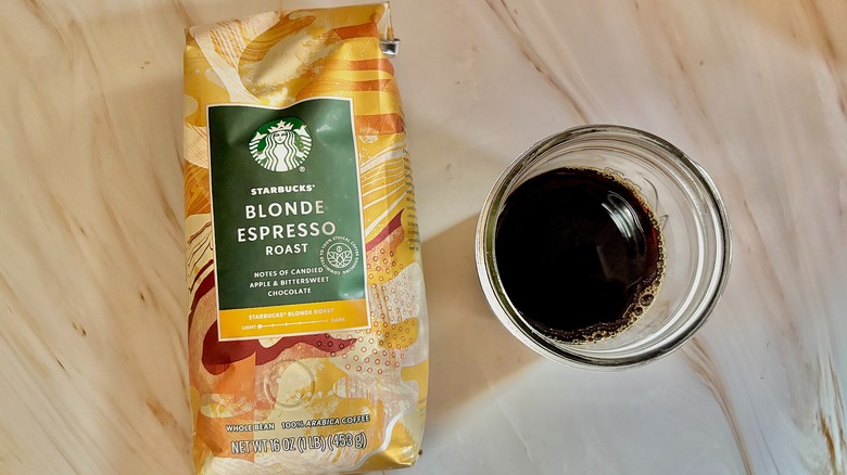 Top-down shot of Starbucks Blonde Espresso bag next to mason jar of cold black coffee