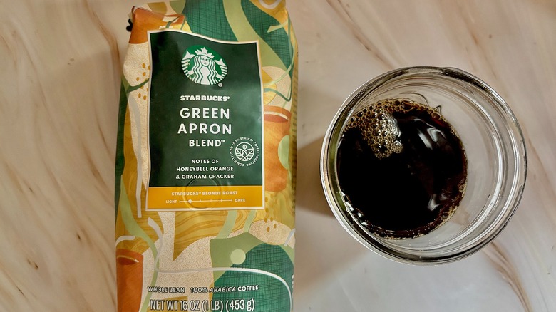 Top-down shot of Starbucks Green Apron bag next to mason jar of cold black coffee