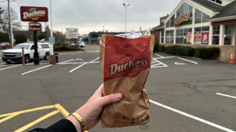 Hand holding paper bag from Duchess restaurant in Duchess parking lot
