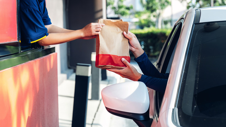 Fast food worker handing bag to customer at drive-thru