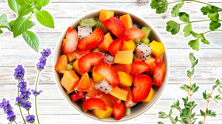 Top-down view of a bowl of fruit surrounded by fresh herbs